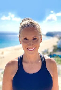 blonde woman is smiling in the camera, she is a health coach and standing at the beach