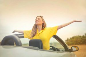 blonde woman sitting in a cabrio car backwards doin a feeling free pose