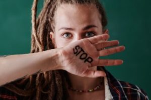 woman with rasta hair holding her hand in front of mouth, on her hand it says stop