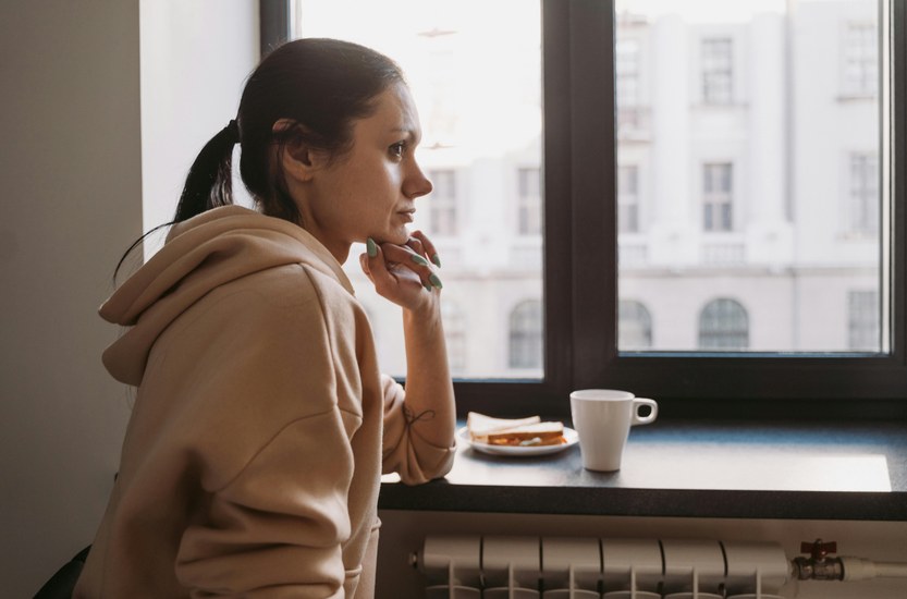 Young woman alone by window in hoodie, reflective mood after quitting weed
