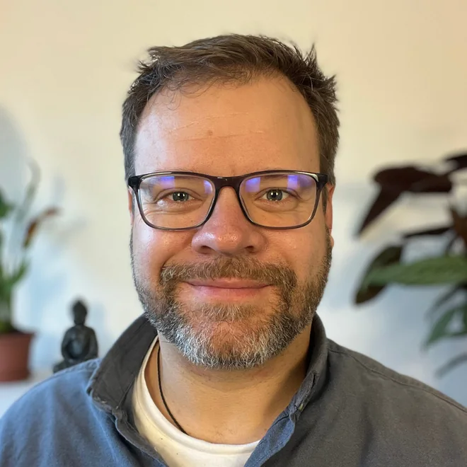 Smiling man with glasses and a grey beard in a room with plants
