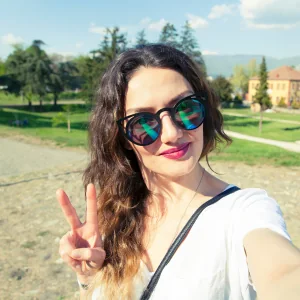 Smiling woman with sunglasses taking a selfie in a park and making a peace sign